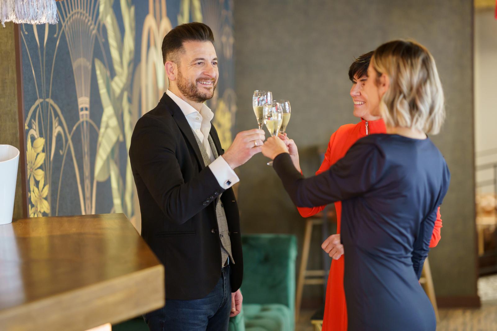 Group of positive well dressed friends clinking glasses with sparkling champagne while celebrating festive event in luxury bar